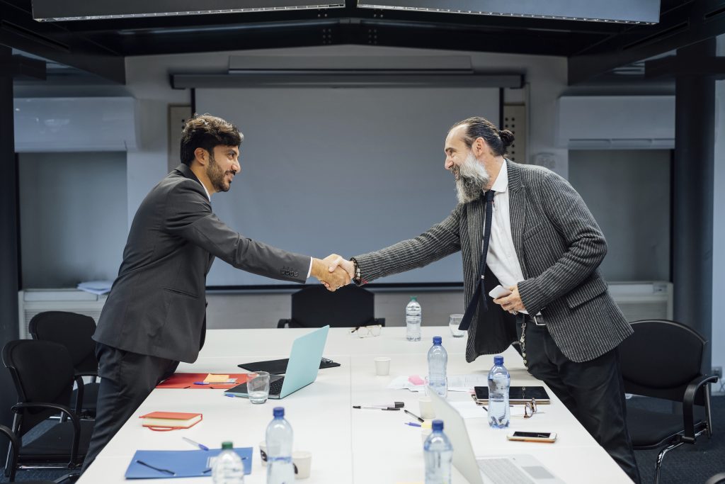 Two businessmen shaking hands over a meeting table, symbolising partnerships in renewable energy solutions.