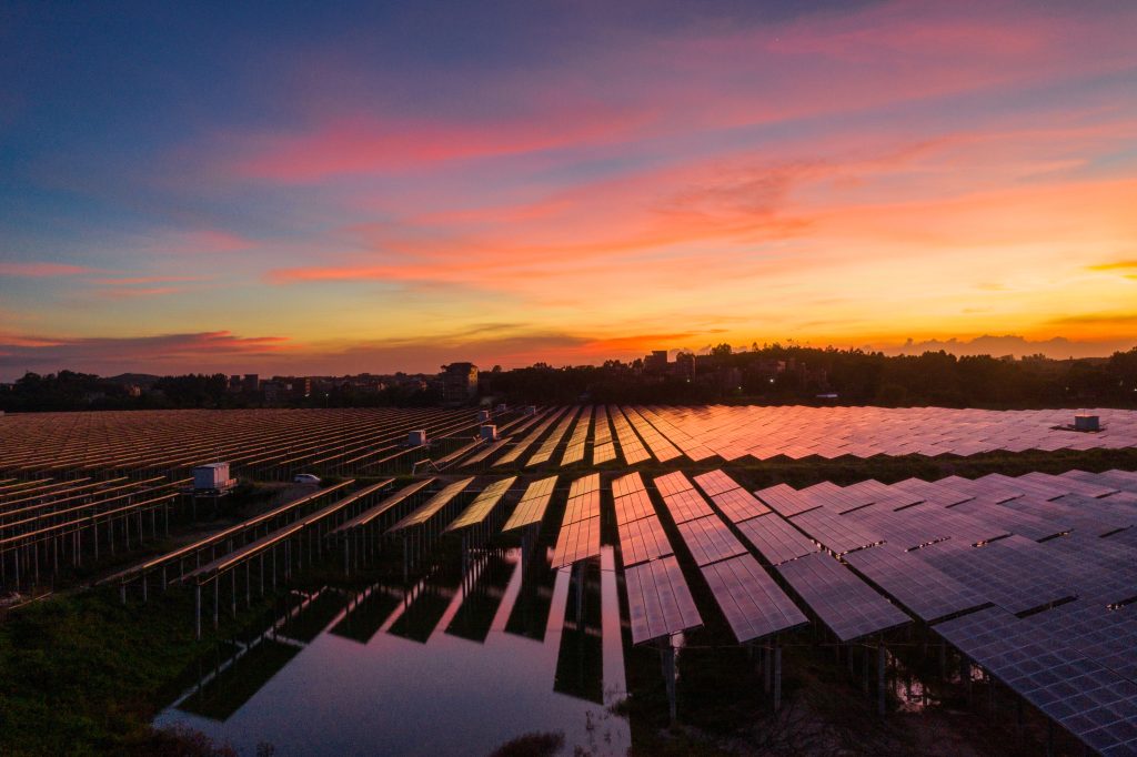 Solar farm at sunset with a reflective water surface, showcasing large-scale renewable energy production.
